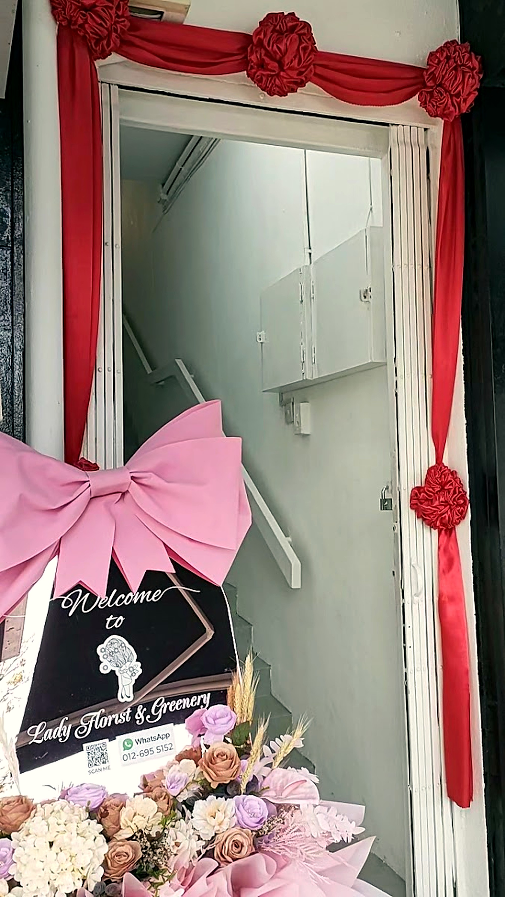 A welcome sign and a bouquet of flowers are displayed in front of an entrance decorated with red fabric and rosettes